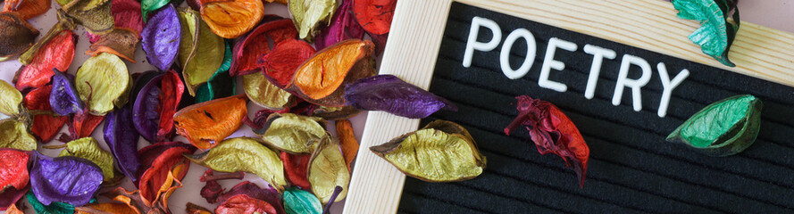 Felt board with the inscription poetry next to a lot of colorful dry leaves and petals. The concept...