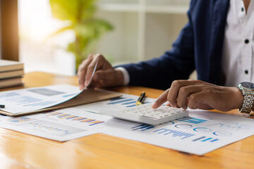 Businessman hand pressing a calculator calculation concept The front view of the hand points to the data from the business data chart to calculate the company's financial analysis.