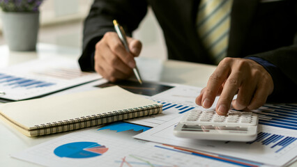 Businessman hand pressing a calculator calculation concept The front view of the hand points to the data from the business data chart to calculate the company's financial analysis.