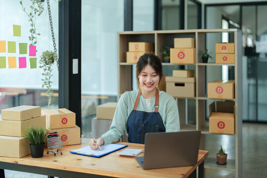 Portrait of a small startup Asian female entrepreneur SME owner checks online orders via computer to take customer orders and pack products into boxes. Online Business Ideas and Freelance