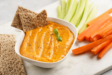 Paprika bell-pepper hummus dip looking like orange pumpkin puree, thin crackers with sesame seeds...