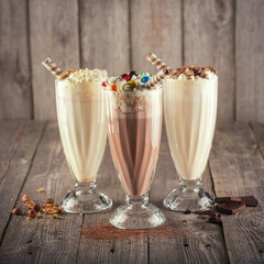 Set of milkshakes in glass with chocolate and vanilla flavors on wooden background.