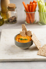 Paprika bell-pepper hummus dip looking like orange pumpkin puree, thin crackers with sesame seeds...