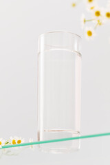 Full glass of natural pure water on a glass shelve with flowers on a blue background. Summer...