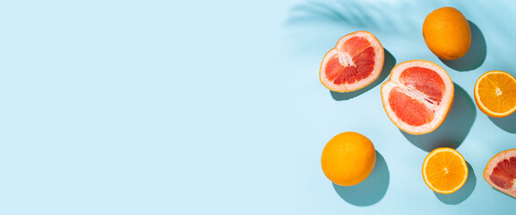 citrus fruits, oranges, grapefruit and the shadow of palm leaves on a blue background. Top view, flat lay. Banner
