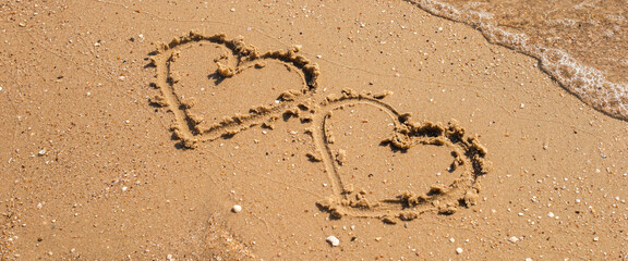 Two hearts drawn on a sandy beach. Top view, flat lay. Banner