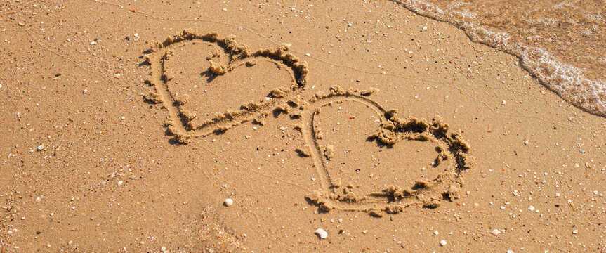 Two hearts drawn on a sandy beach. Top view, flat lay. Banner