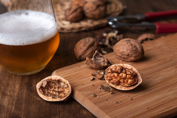 Cracked walnuts on a wooden board next to a glass of beer. Close-up.