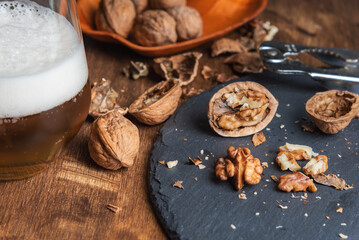 Cracked walnuts on a stone plate next to a glass of beer. Close-up.