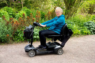Blond haired woman on mobility scooter smiles happily as she enjoys the freedom being outdoors on a spring day that the scooter allows her despite her disability.