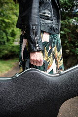 Close up of woman arm holding a guitar case in a park.