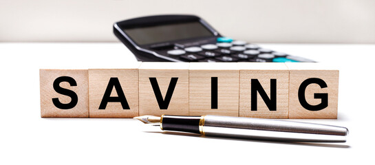 Obraz premium The light table has a black calculator, a fountain pen, and wooden cubes with the text SAVING. Business concept