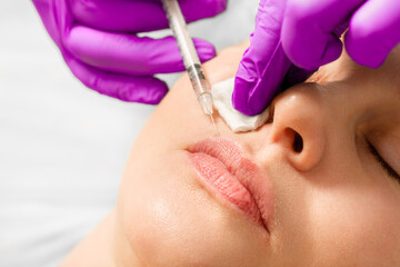 A woman makes lip shape correction in a cosmetology clinic. Lips injections, lip augmentation.
