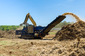 Fototapeta na wymiar A hydraulic crane loading for shredding machine in roots wood chopped wooding material