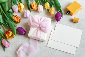 Colorful spring mockup of bright tulips, perfume, and card on a neutral background.