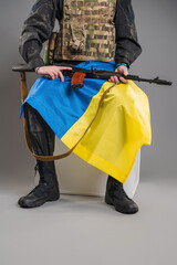 A soldier sits with a weapon and with a Ukrainian flag on his hands