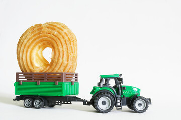 Green toy tractor is carrying a large round donut in a trailer. The concept of delivering products...