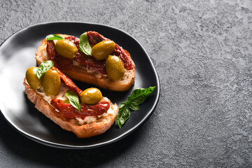 Bruschetta with sun dried tomatoes. Toast or sandwich with ricotta, sun dried tomatoes and Provence herbs with basil servered on black plate on black background table. Selective focus.