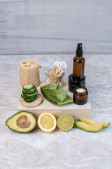 Naklejka premium Braunglasflasche und Tiegel mit Creme, hausgemachte Gesichtspflege, natürlich, mit Gurke, Avocado, Aloe Vera, Limette und Zitrone, feuchtigkeitsspendende Gesichtspflege, Q-Tips aus Bambus