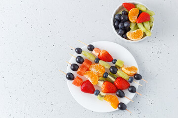 Fresh fruit skewers on a plate for a healthy snack on a gray background. copy space