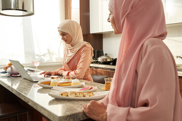 Muslim women using modern notebook in kitchen