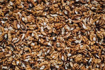 Background, texture of a pile of brown pieces of walnuts made of wood, peeled nuts lying on a wooden table. Food photography, top view.