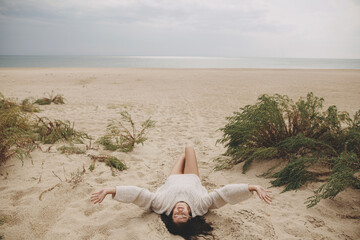Beautiful woman lying on sandy beach on background of green grass and sea, carefree tranquil...