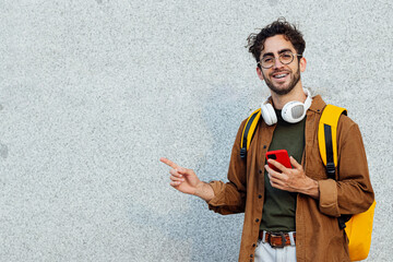 Outdoor portrait of handsome young hipster man with mobile phone pointing aside.