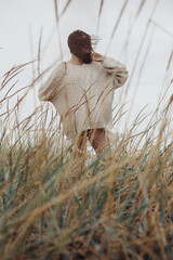 Beautiful stylish woman with windy hair in knitted sweater posing among wild grass. Carefree...