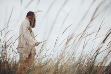 Beautiful stylish woman with windy hair in knitted sweater posing among wild grass. Carefree...