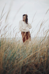 Beautiful stylish woman with windy hair in knitted sweater posing among wild grass. Carefree...