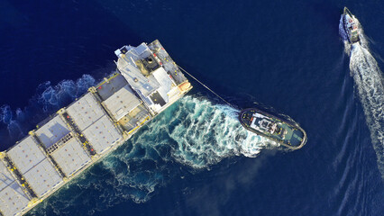Aerial drone top down photo of tow - tug boat assisting by pulling empty container ship to depart...
