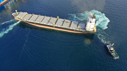 Aerial drone top down photo of tow - tug boat assisting by pulling empty container ship to depart...