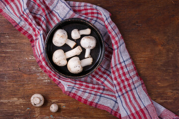 Wooden bowl of fresh raw champignon mushrooms on red kitchen towel. Autumn harvest, seasonal jrganic vegan food, healhty eating habits.