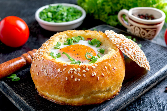 Bun stuffed with egg, fresh herbs on a black background. The concept of breakfast, recipes from eggs.