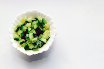 Sliced cucumber in a cube for salad in a plate on a white table.