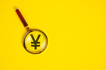 Yuan symbol under magnifying glass, on yellow background.