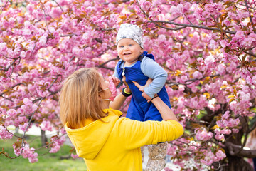 Mother in medical mask with little son playing in the park the sakura tree