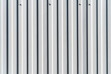 White painted panel with nails texture corrugated iron aluminum vertical stripes contrasting with the shadow from the side lighting of the afternoon sun.