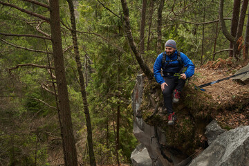 Naklejka premium Tourist resting on cliff in forest during walking tour