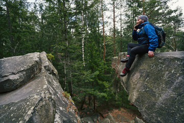 Foot traveller taking phone call on rock in forest