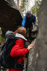 Positive tourist helping woman pass difficult area of trekking path