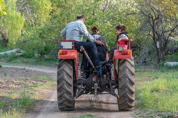 Back view with selective focus of grandpa, mother and little girl strolling with tractor.