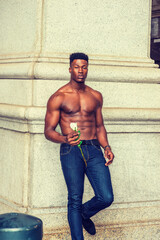 African American Man seeking love in New York. Shirtless, half naked, waring blue jeans, a young, strong, sexy guy standing by column on street, holding white rose, thinking.  filtered effect..