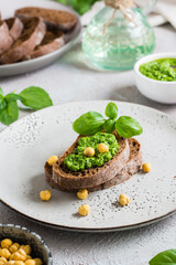 Fresh sandwich with pesto and chickpeas on rye bread on a plate on the table. Vertical view