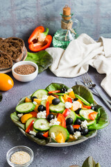 Greek salad of tomatoes, cucumbers, peppers, olives, lettuce and cheese on a plate.  Vertical view