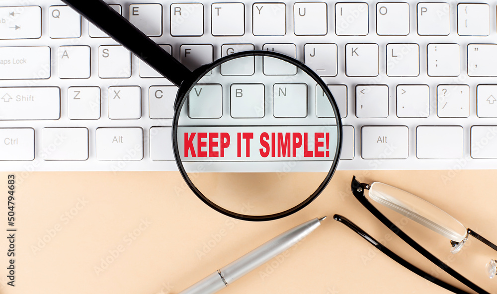 Aufkleber text keep it simple on keyboard with magnifier , glasses and pen on beige background