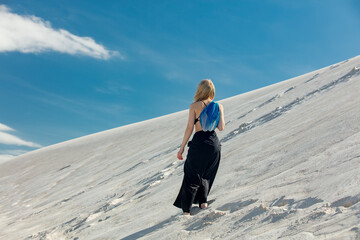 Woman with blue net bag walking on white sand dune in desert in summer