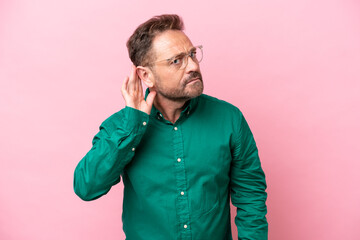 Middle age caucasian man isolated on pink background listening to something by putting hand on the...