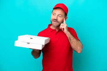 Pizza delivery man with work uniform picking up pizza boxes isolated on blue background thinking an...